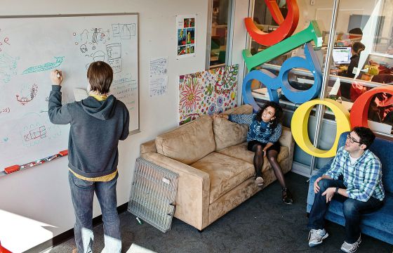 Persona en una oficina de Google escribiendo en una pizarra mientras otras lo miran